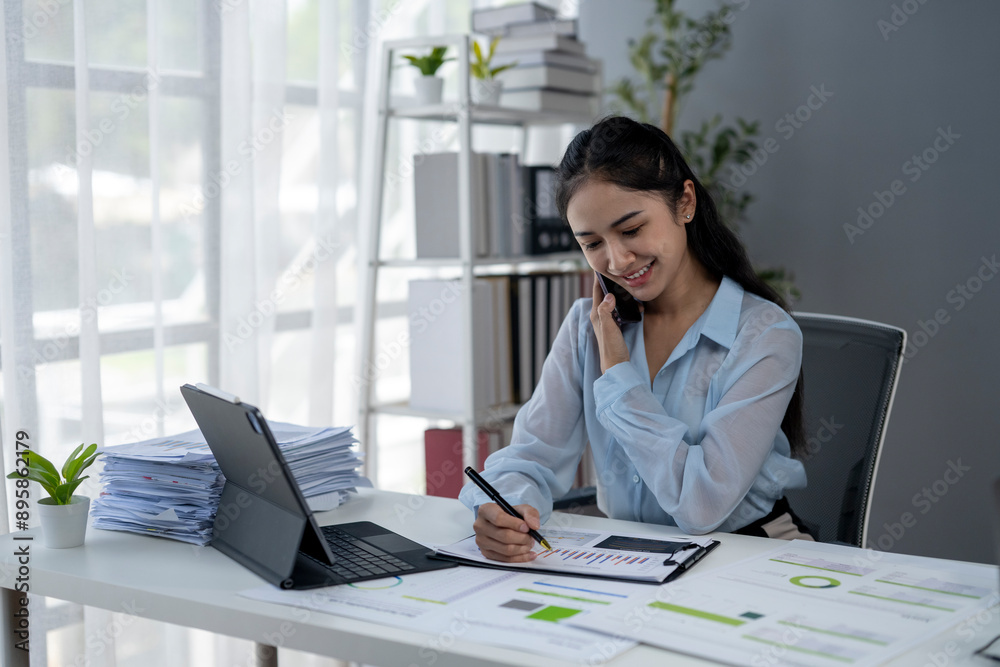 A woman is talking on her cell phone while sitting at a desk with a laptop A woman is talking on her cell phone while sitting at a desk with a laptop