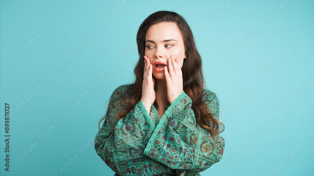 Shocked young woman covers mouth in blue studio