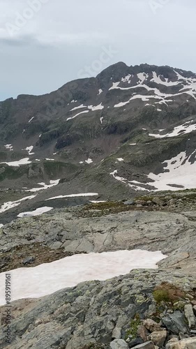 Lac blanc vu de haut, entouré par une montagne dont la pente est à moitié enneigée. La neige contraste avec les parties dénudées, créant un paysage alpin spectaculaire et glacé.