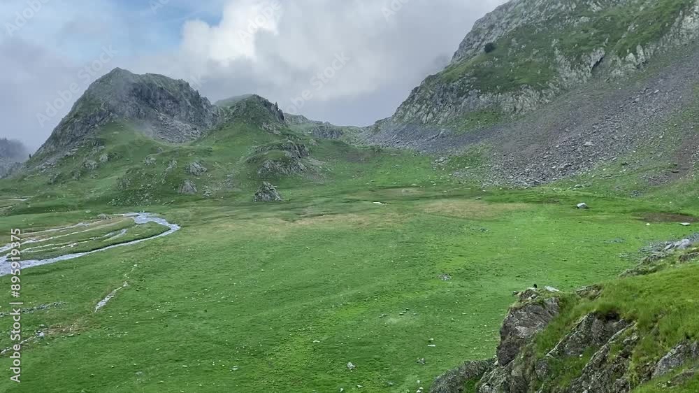 Une petite rivière serpente à travers une plaine de montagne, entourée de sommets majestueux. L'eau scintille sous le ciel clair, offrant un contraste paisible avec les montagnes environnantes.