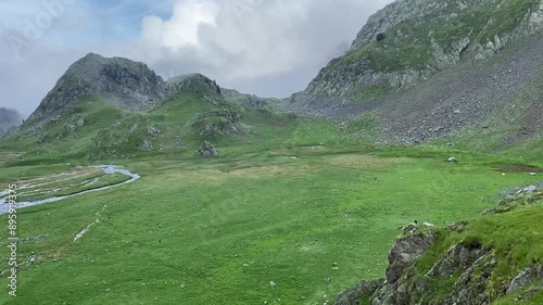 Une petite rivière serpente à travers une plaine de montagne, entourée de sommets majestueux. L'eau scintille sous le ciel clair, offrant un contraste paisible avec les montagnes environnantes.