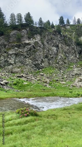 Une petite rivière serpente à travers une plaine de montagne, entourée de sommets majestueux. L'eau scintille sous le ciel clair, offrant un contraste paisible avec les montagnes environnantes.