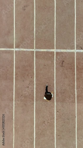 A curly-haired girl runs along the sports ground. Top view. Shooting from a drone. Vertical video