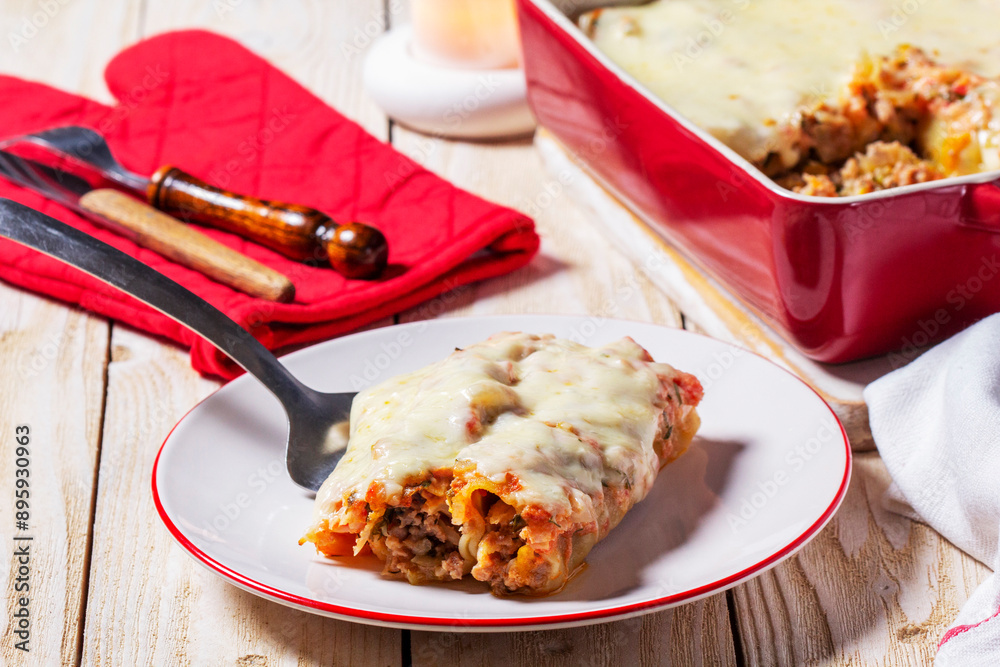 Cannellone with meat filling, tomato sauce and cheese on a light wooden table.
