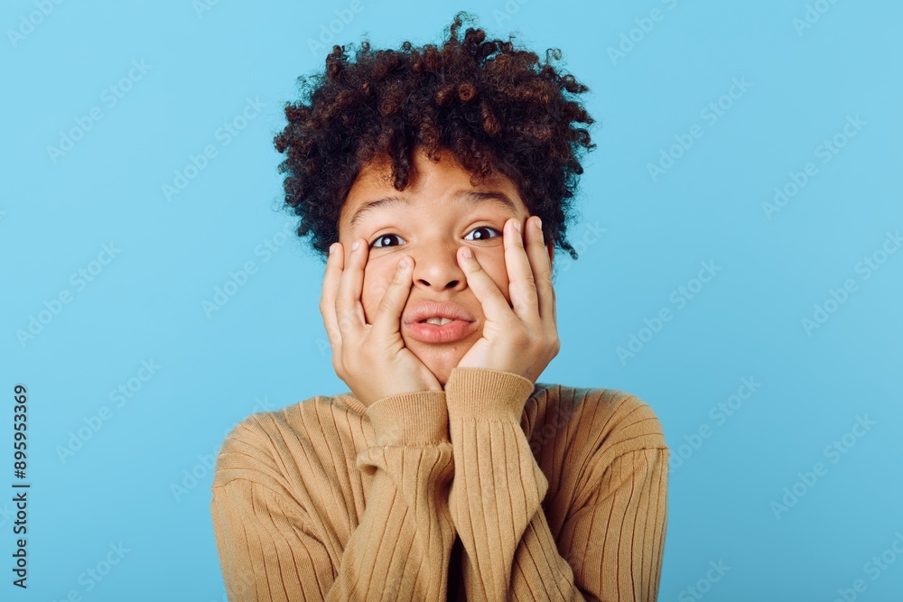 young african american girl hiding her face with her hands against a bright blue backdrop in shy gesture young african american girl hiding her face with her hands against a bright blue backdrop in shy gesture