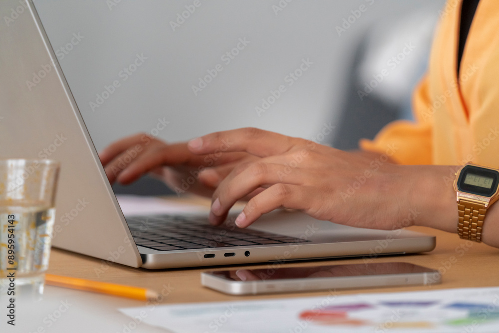 A close-up of hands typing on a laptop with a glass of water and a smartphone nearby. The image portrays a productive workspace equipped with essential tools for efficient work. A close-up of hands typing on a laptop with a glass of water and a smartphone nearby. The image portrays a productive workspace equipped with essential tools for efficient work.