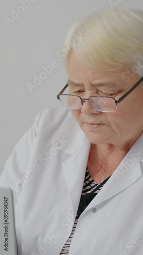 Vertical Screen: Experienced woman doctor checking patients history in laptop while sitting at desk in hospital office. Nurse in charge working on computer at workplace. photo