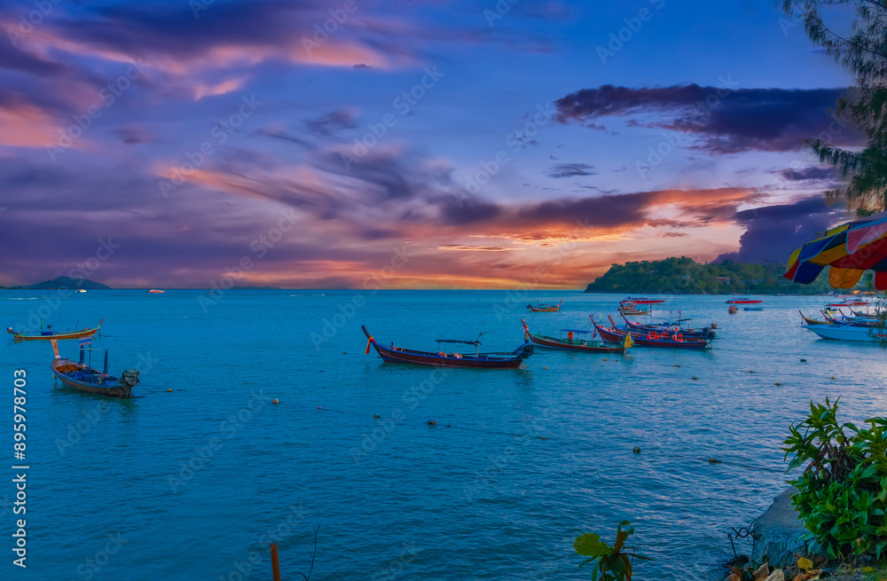 Colourful Skies Sunset over Rawai Beach in Phuket island Thailand. Lovely turquoise blue waters, lush green mountains colourful skies and beautiful views of long tail Boats Colourful Skies Sunset over Rawai Beach in Phuket island Thailand. Lovely turquoise blue waters, lush green mountains colourful skies and beautiful views of long tail Boats