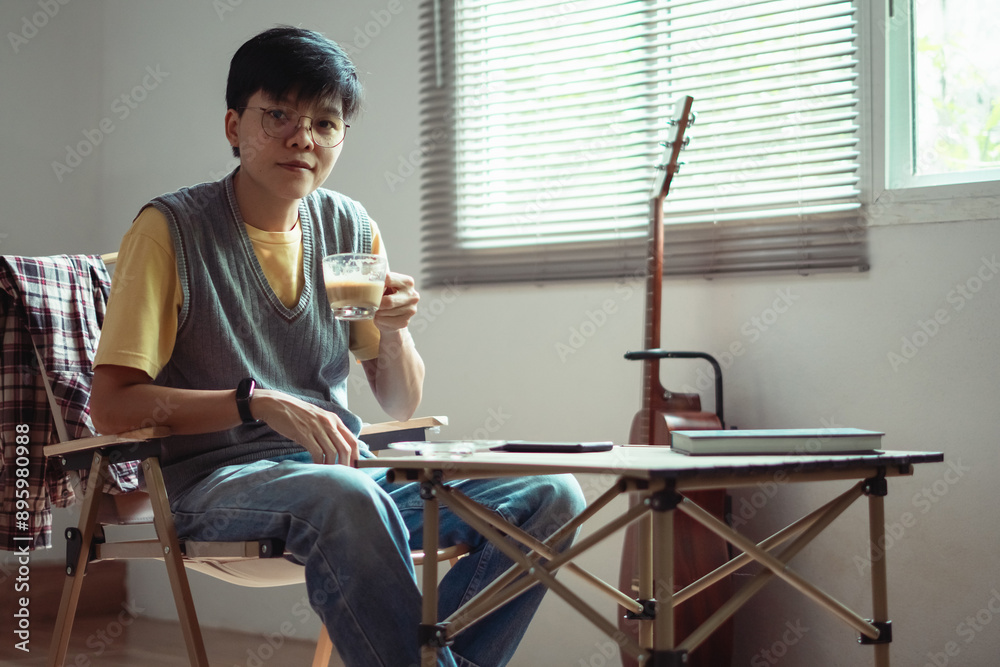 Fototapeta premium Asian embracing LGBTQ identities, smile warmly at the camera, enjoying coffee and guitar near window capturing a joyful and inclusive moment of their lifestyle at home.