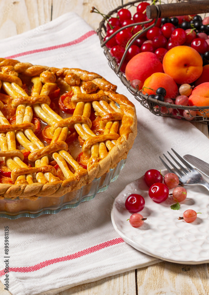 Apricot pie decorated with dough ornament and a metal basket with fruits and berries.
