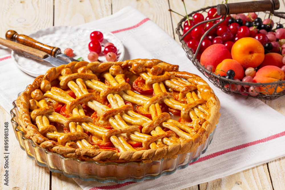 Apricot pie decorated with dough ornament and a metal basket with fruits and berries.