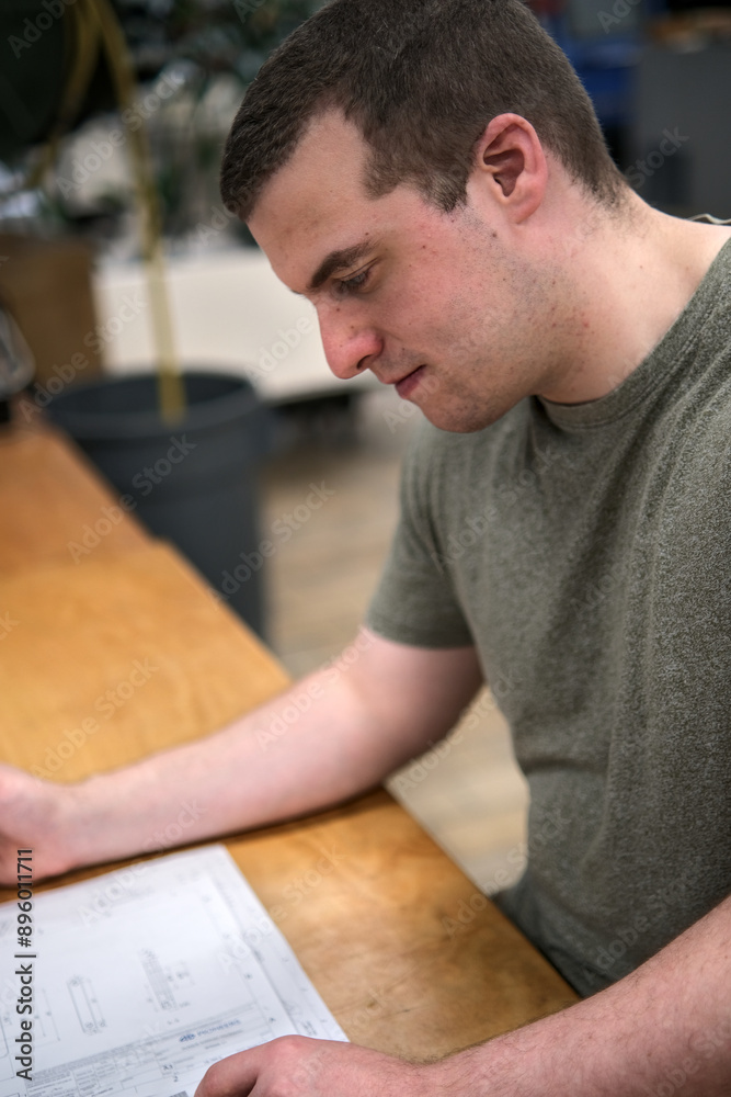 Side view of a Caucasian man, wearing a T-shirt and studying a mechanical drawing, in a workshop. Side view of a Caucasian man, wearing a T-shirt and studying a mechanical drawing, in a workshop.