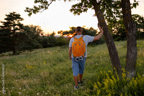 A male tourist is looking at the sunset and holding a tree.