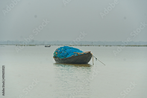 picture of a black colored wooden boat floating in the middle of a lake with blue colored fishing net piled over it