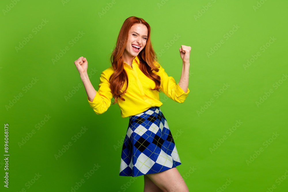 Photo portrait of lovely young lady raise fists winning dressed stylish yellow garment isolated on green color background