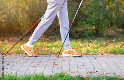 Legs of woman in sport wear and with walking sticks for popular Nordic walking in the autumnal park. Scandinavian trekking sticks hiking, exercising, healthy lifestyle. Copy space, empty space.
