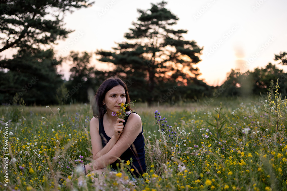 Beautiful young dreamy girl is sitting in nature and holding a bouquet of wildflowers Beautiful young dreamy girl is sitting in nature and holding a bouquet of wildflowers