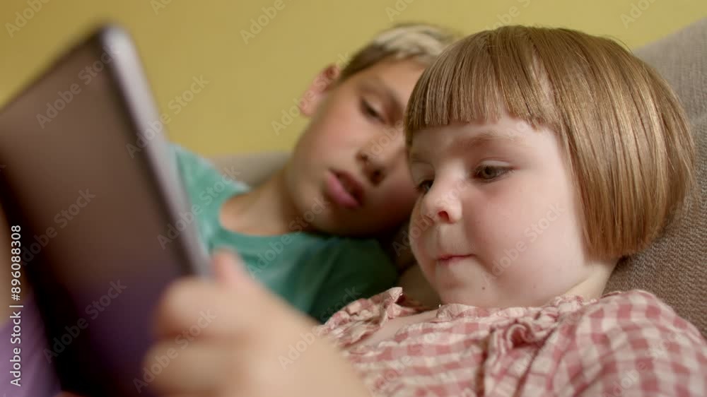 Tablets offer a wide range of entertainment content - games, movies and music - that are attractive to children of all ages. Brother and sister are looking at the tablet. Tablets offer a wide range of entertainment content - games, movies and music - that are attractive to children of all ages. Brother and sister are looking at the tablet.