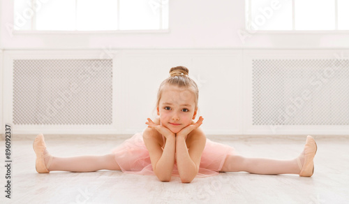 Little ballerina in split on floor, copy space. Smiling baby girl dreaming to become professional ballet dancer, classical dance school photo