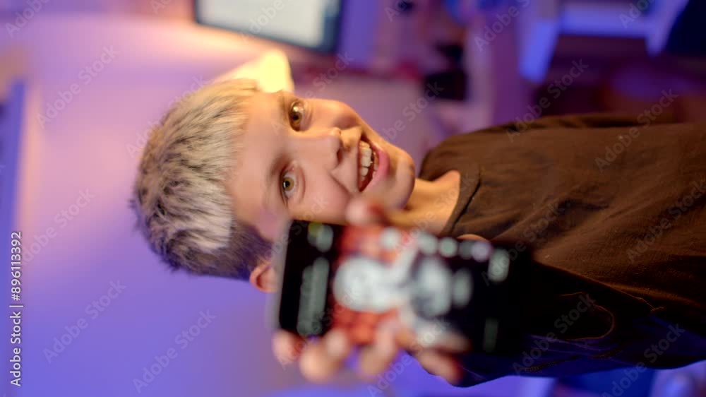 Smile boy is displaying his smartphone against a blurred background, exuding a modern tech atmosphere indoors