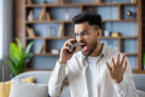 Fotografía Angry man shouting on phone in modern living room expressing frustration and str