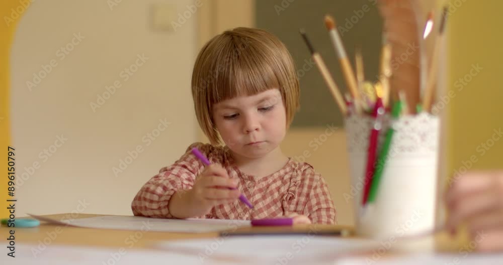 A young girl concentrating on drawing with purple pencil, surrounded by various art supplies on the table. A young girl concentrating on drawing with purple pencil, surrounded by various art supplies on the table.