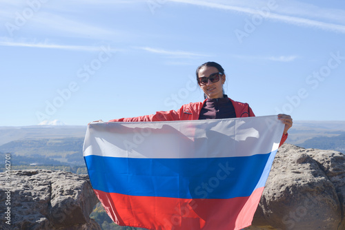 The Russian flag is on the shoulders of a girl standing against the backdrop of the Caucasus mountains. Unity Day in Russia.