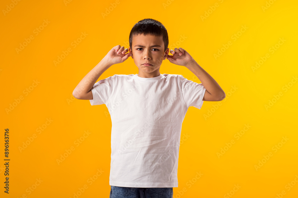 Kid boy covering ears over yellow background. Noise, stress and childhood concept Kid boy covering ears over yellow background. Noise, stress and childhood concept