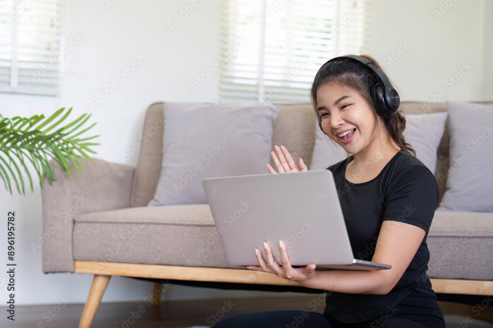 Young Woman Using Laptop and Headphones for Video Call at Home, Smiling and Waving Young Woman Using Laptop and Headphones for Video Call at Home, Smiling and Waving