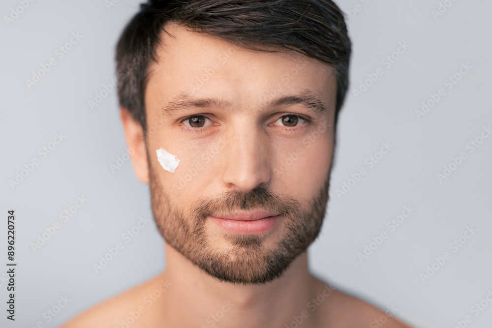 A man with a beard applies facial moisturizer to his cheek. A man with a beard applies facial moisturizer to his cheek.