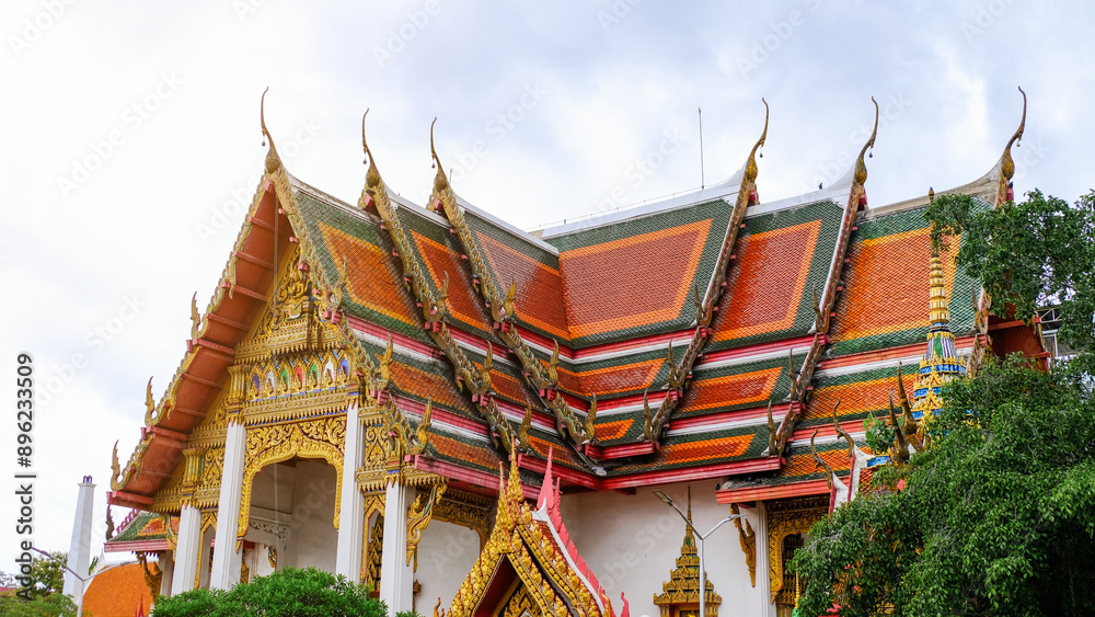 Fototapeta premium A stunning view of a traditional Thai temple adorned with vibrant colors and intricate architecture under a cloudy sky.