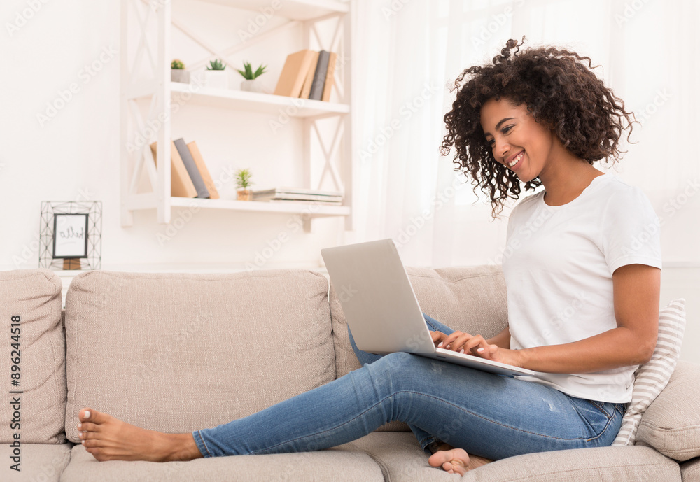 African-american woman working on laptop computer, sitting on sofa at home, copy space African-american woman working on laptop computer, sitting on sofa at home, copy space