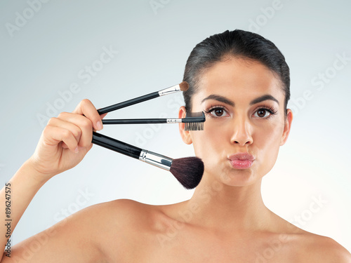 Portrait, makeup brush and woman pout in studio for cosmetic application, beauty transformation and salon glow. Female person, facial shine and product tools for aesthetic makeover on blue background