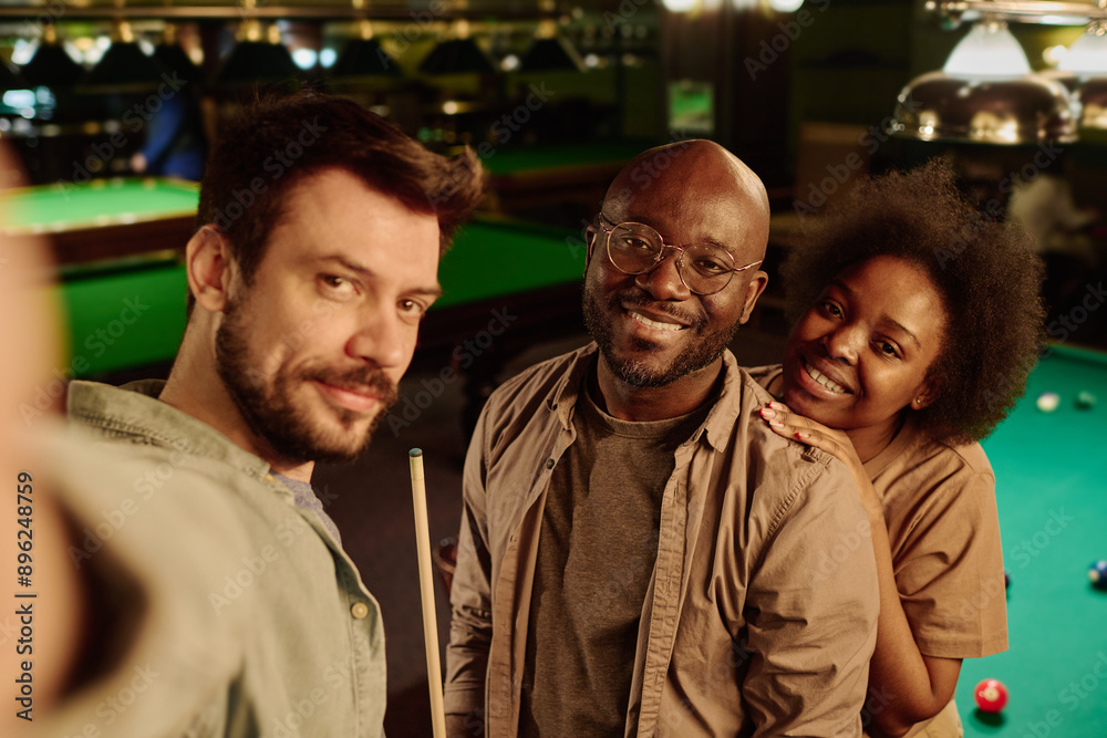 Happy young affectionate African American couple and their friend looking at smartphone camera while bearded man taking picture Happy young affectionate African American couple and their friend looking at smartphone camera while bearded man taking picture