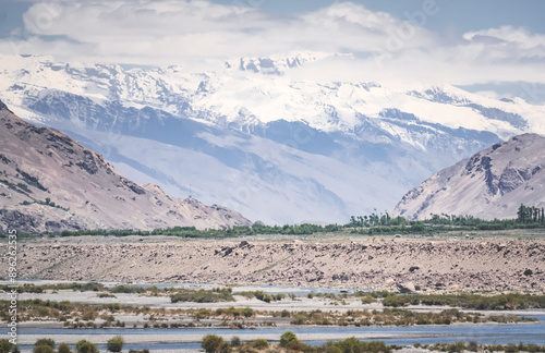 Pyanj River flows in Wakhan Valley among rocky high mountains against snow-capped peaks and glaciers in Tajikistan's Tien Shan mountains, landscape for background photo