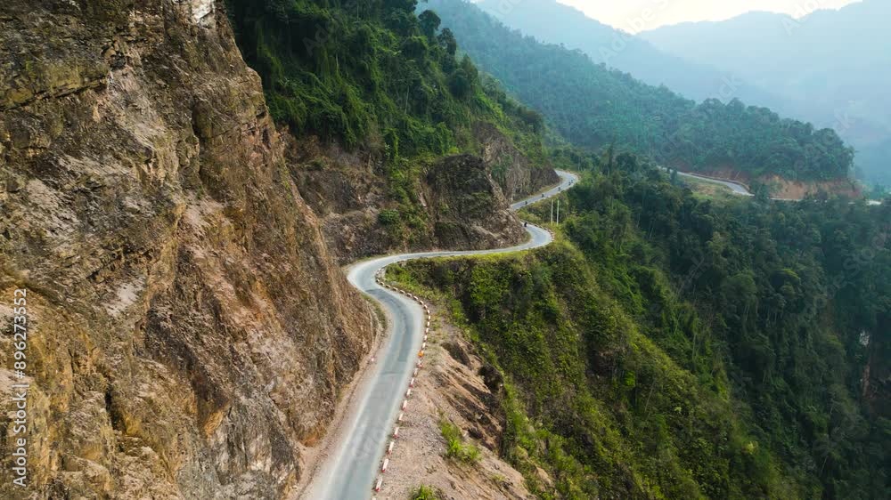 Aerial view of a dangerous winding road along a lush green mountain cliff leading to the Ha Giang Loop in Vietnam