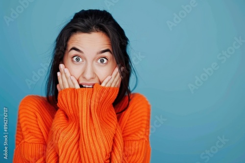 A young woman in an orange sweater playfully covers her face with her hands photo