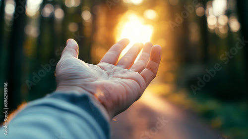 Close up of a hand stretches out towards the warm glow of the setting sun in a tranquil forest path.