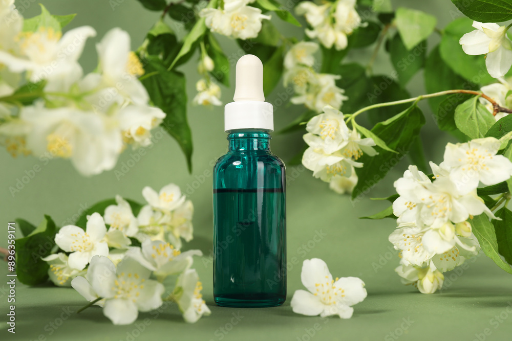 Essential oil in bottle and beautiful jasmine flowers on pale green background Essential oil in bottle and beautiful jasmine flowers on pale green background