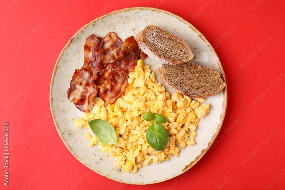 Delicious scrambled eggs with bacon and basil in plate on red background, top view Delicious scrambled eggs with bacon and basil in plate on red background, top view