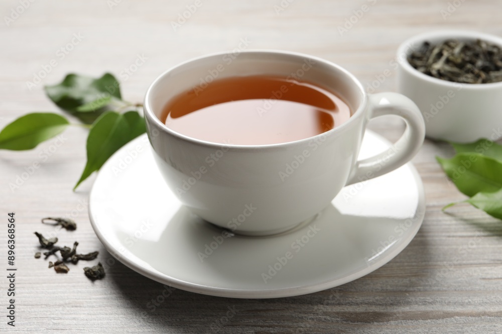 Refreshing green tea in cup and leaves on grey wooden table, closeup Refreshing green tea in cup and leaves on grey wooden table, closeup