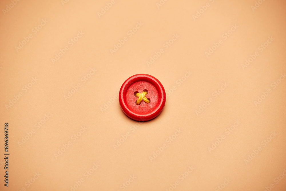 One alone red clothes button with a yellow rope cross isolated on the bright solid fond plain sandy beige background One alone red clothes button with a yellow rope cross isolated on the bright solid fond plain sandy beige background