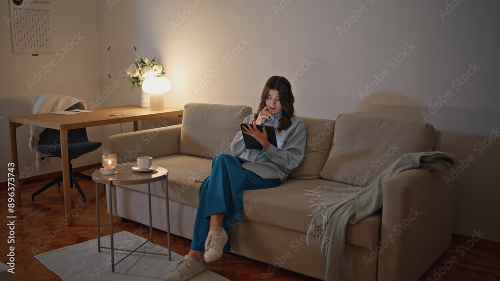 Businesswoman reading tablet evening at room. Serious woman working sitting sofa Businesswoman reading tablet evening at room. Serious woman working sitting sofa