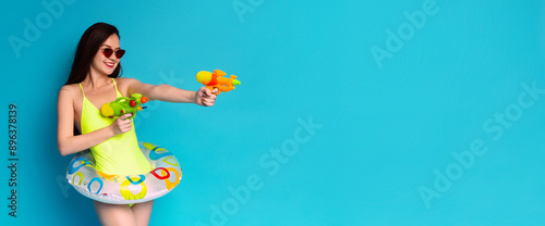 Принти на полотні A woman in a bright yellow swimsuit and sunglasses holds two water guns, one in each hand
