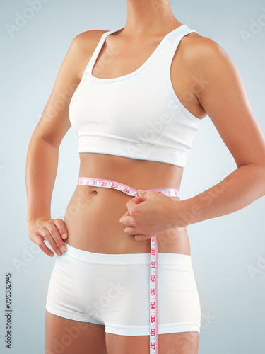 Woman, hands and tape measure on abdomen in studio for tracking weight loss of thermogenesis and progress. Girl, white background and monitor calorie burn of metabolic booster and appetite control.