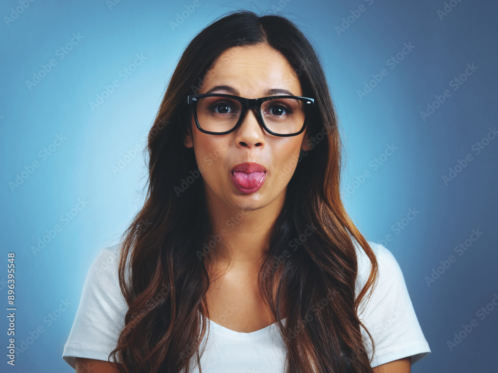 Obraz premium Woman, happy and glasses portrait with tongue for silly action, feeling goofy and geek in studio. Female person, crazy face and eyewear with comedy for confidence, funny and nerd by blue background