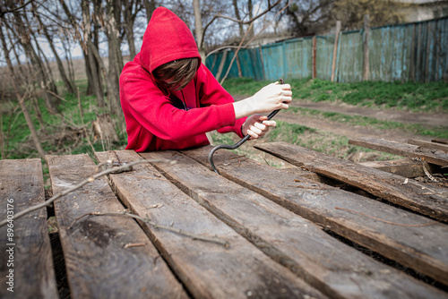 Person in Red Hoodie Using a Crowbar to Pry Up Wooden Boards Outside