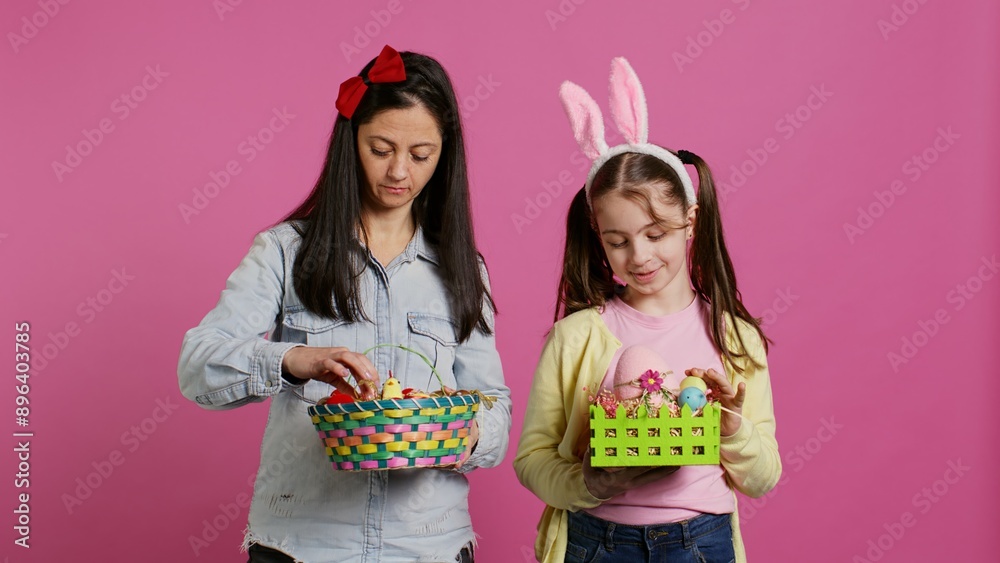 Joyful confident child and mother showing easter baskets on camera, decorating festive arrangements for spring holiday. Happy schoolgirl with bunny ears posing with her mom in studio. Camera B. Joyful confident child and mother showing easter baskets on camera, decorating festive arrangements for spring holiday. Happy schoolgirl with bunny ears posing with her mom in studio. Camera B.