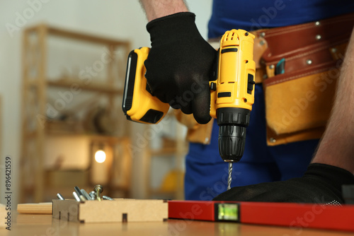 Craftsman working with drill at wooden table in workshop, closeup