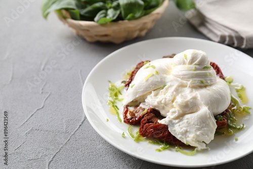 Delicious burrata cheese and sun-dried tomatoes on light grey table, closeup. Space for text